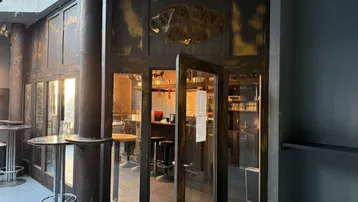 Eingangsbereich einer Bar mit rustikalen Holztüren und Glasfront, die in den Hauptraum führt.