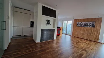 Heller Wohnbereich mit Holzboden, Holzwandverkleidung und einem modernen Kamin als Raumteiler.