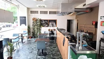 Geräumiger Gastraum einer Pizzeria mit Tischen, Stühlen, Theke und Blick auf die Straße durch große Fenster.