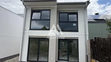 Moderne Neubaufassade mit großen Fenstern und Schiebetüren, umgeben von Kiesflächen.