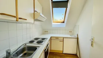 Kleine Küche mit Dachschräge, Einbauschränken, Spüle, Elektroherd und Dachfenster.