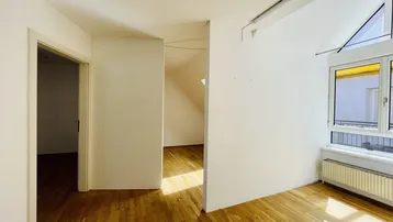 Helles Wohnzimmer mit Holzboden, weißen Wänden und Dachschräge.