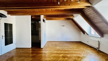 Geräumiges Dachgeschosszimmer mit sichtbaren Holzbalken, Dachschrägen und Fischgrätparkettboden.