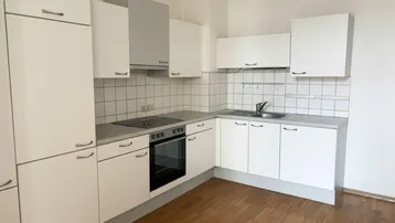 Helle Einbauküche mit weißen Schränken, Holzfußboden und modernen Geräten.