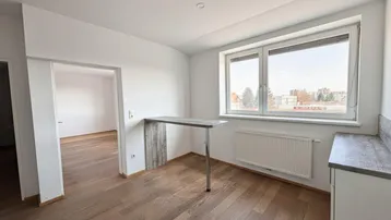 Heller Raum mit Holzboden, großen Fenstern und einer Theke, die zu einem weiteren Zimmer führt.