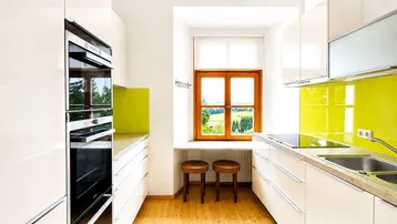 Moderne Küche mit weißen Hochglanzfronten, integrierten Geräten und einem Fenster mit grüner Aussicht.