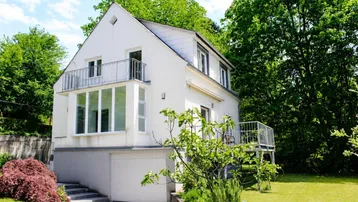 Weißes Einfamilienhaus mit Balkonen, Garage und gepflegtem Gartenbereich unter blauem Himmel.