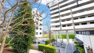 Blick auf moderne Wohngebäude mit Balkonen und einem begrünten Innenhof mit Sitzgelegenheiten.