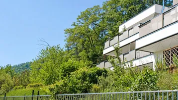 Moderne Wohnanlage mit Balkonen, eingebettet in eine grüne Hanglage mit üppiger Vegetation.