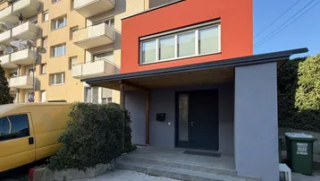 Moderne Hausfassade mit rotem Putz und überdachtem Eingangsbereich, umgeben von Grün.