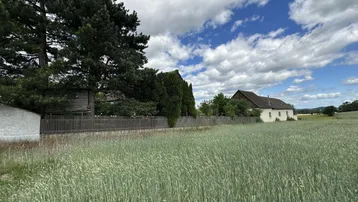 Ländliche Ansicht eines Feldes mit einem traditionellen Gebäude im Hintergrund unter blauem Himmel.