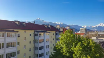 Panoramablick auf schneebedeckte Berge, umgeben von Gebäuden und grünen Bäumen.