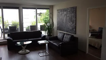 Helles Wohnzimmer mit dunklen Sofas, Holzboden und großen Fenstern zur Terrasse.