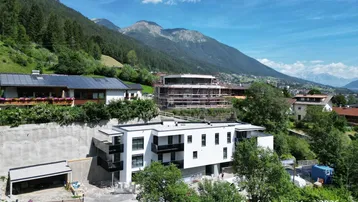 Neubauprojekt in alpiner Umgebung mit Blick auf die Berge und umliegende Häuser.
