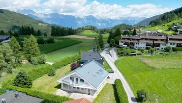 Luftaufnahme eines modernen Hauses in einer malerischen Berglandschaft mit grünen Feldern.