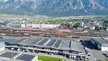 Luftaufnahme eines Gewerbegebiets mit Bergen im Hintergrund und Photovoltaikanlagen auf den Dächern.