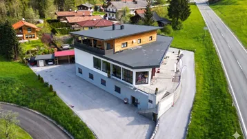 Modernes Gebäude mit Flachdach und großer Dachterrasse in ländlicher Umgebung.