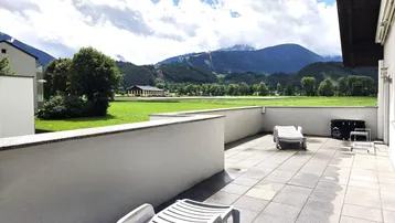 Große geflieste Terrasse mit Liegestühlen und weitem Blick auf die umliegende Berglandschaft und grüne Felder.