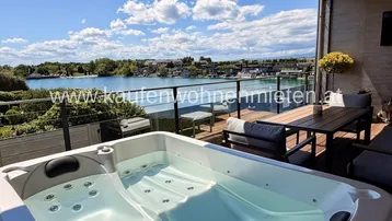 Geräumige Terrasse mit Whirlpool, Essbereich und atemberaubendem Seeblick unter blauem Himmel.