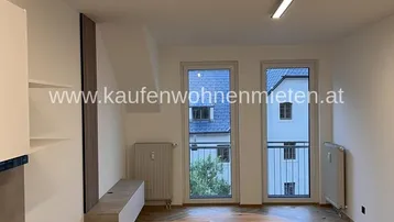 Wohnbereich mit Fischgrätparkett und Zugang zu einem französischen Balkon mit Blick ins Grüne.
