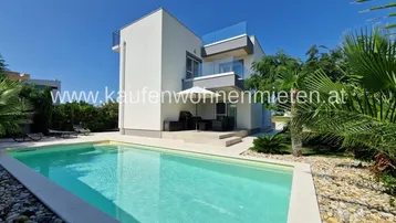 Moderne Villa mit privatem Pool, Sonnenterrasse und mediterraner Bepflanzung unter blauem Himmel.