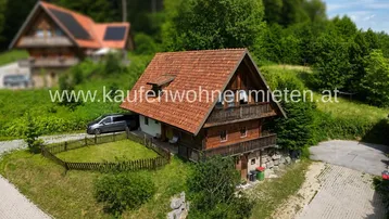 Traditionelles Holzhaus im Chalet-Stil mit Satteldach, Balkonen und umgeben von viel Grün.