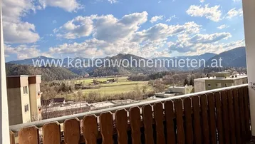 Sonniger Balkon mit rustikalem Holzzaun und weitreichendem Panoramablick auf die Berge.