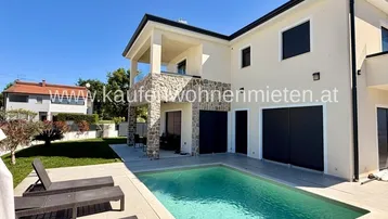 Modernes Haus mit privatem Pool, Sonnenterrasse und Steinverkleidung unter blauem Himmel.
