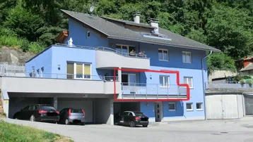 Modernes blaues Wohnhaus mit Satteldach, mehreren Balkonen und integrierter Garage, umgeben von viel Grün.