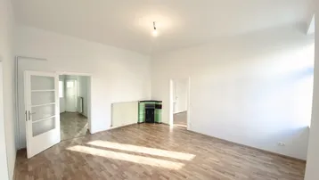 Geräumiges Zimmer mit Parkettboden und einem traditionellen Kachelofen als Blickfang.