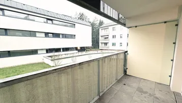 Balkon mit Fliesenboden und Blick auf die umliegenden Gebäude und eine kleine Grünfläche.