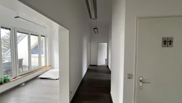 Heller Flur mit dunklem Laminatboden und Zugang zu verschiedenen Räumen, inklusive WC-Schild.