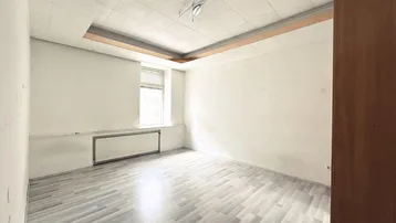 Helles Zimmer mit Laminatboden und einem Fenster, das viel Tageslicht hereinlässt.