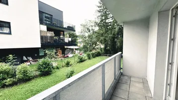 Balkon mit Fliesenboden und Blick auf den Gemeinschaftsgarten und angrenzende Gebäude.