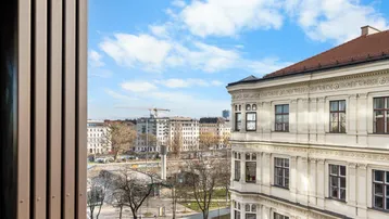 Blick aus dem Fenster auf eine belebte Stadtstraße mit historischen Gebäuden und einem Baukran am Horizont.