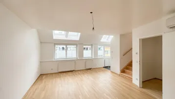 Helles Wohnzimmer mit Holzparkettboden, Dachfenstern und Zugang zu einer Holztreppe.