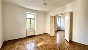 Helles Zimmer mit Fischgrätparkett, hohen Decken und Flügeltüren zu einem weiteren Raum.