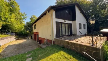 Freistehendes Haus mit heller Fassade, dunklen Holzdetails und einer gepflasterten Terrasse.