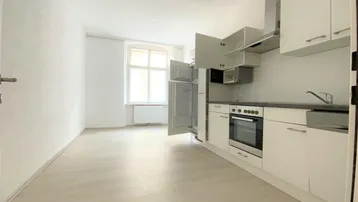 Helle, offene Küche mit weißer Einbauküche, modernen Geräten und hellem Laminatboden.