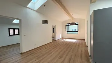 Helles Wohnzimmer mit Holzbalken, Dachfenster und Laminatboden in einem modernen Neubau.