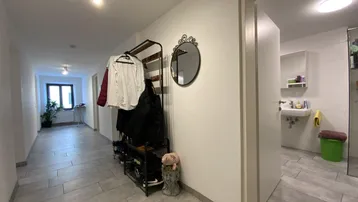 Heller Flur mit Garderobe, Spiegel und Zugang zu weiteren Räumen, ausgestattet mit modernen Fliesen.