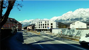 Moderne Architektur an einer Straße mit schneebedeckten Bergen im Hintergrund unter blauem Himmel.