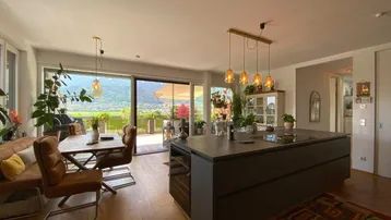 Offener Wohnbereich mit moderner Küche, Essbereich und Zugang zur Terrasse mit Bergblick.
