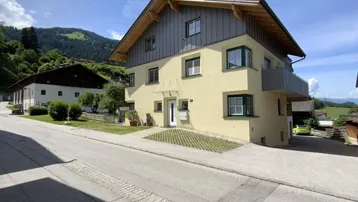 Wohnhaus mit gelber Fassade und Holzdach, gelegen an einer ruhigen Straße mit Bergblick.