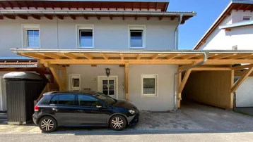 Modernes Haus mit Holzcarport und gepflasterter Einfahrt unter blauem Himmel.