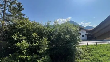 Panoramablick auf die grüne Landschaft mit Bergen und einem Gebäude im Hintergrund.