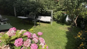 Gepflegter Garten mit blühenden Hortensien, Schaukel und Photovoltaikanlage auf dem Dach des Hauses.