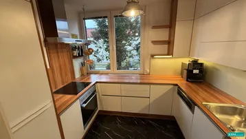 Moderne Küche mit Holz-Arbeitsplatten, weißen Schränken und Blick ins Grüne durch das Fenster.