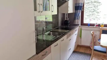 Funktionale Küche mit weißen Schränken, dunkler Arbeitsplatte und Essbereich am Fenster.