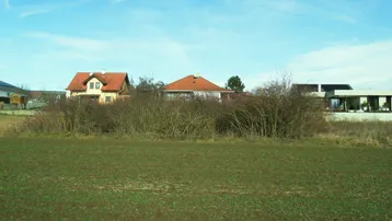 Weitläufiges Feld mit Blick auf Wohnhäuser und den blauen Himmel.